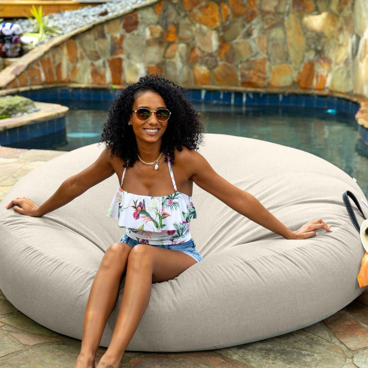 Woman sitting poolside on the Jaxx Cocoon Outdoor bean bag in Flax fabric, weatherproof outdoor seating