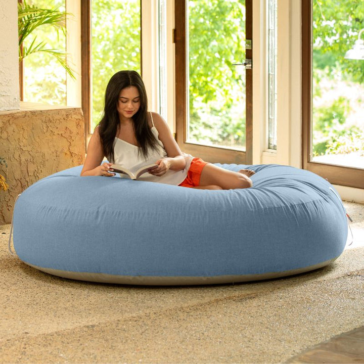 Woman reading on the Jaxx Cocoon Outdoor bean bag in Ocean Blue fabric, oversized deep pressure seating indoors