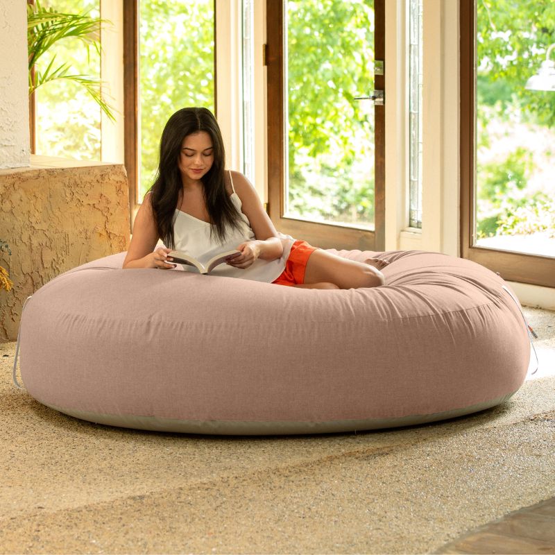 Woman reading on the Jaxx Cocoon Outdoor bean bag in Petal fabric, oversized deep pressure seating indoors