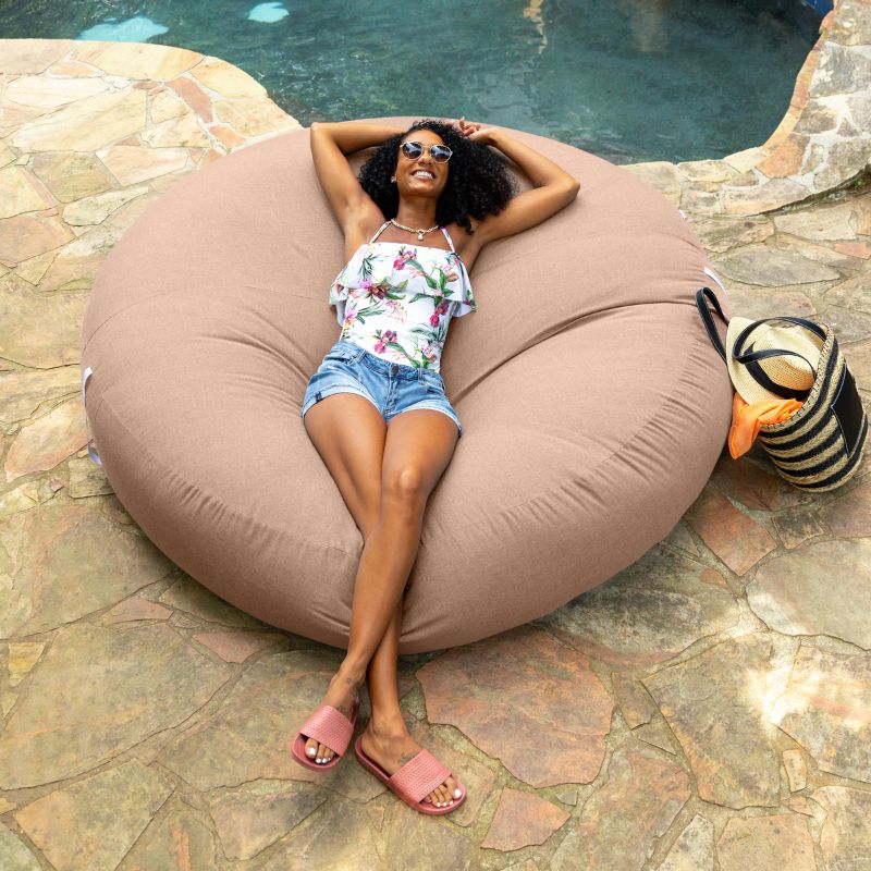 Woman relaxing poolside on the Jaxx Cocoon Outdoor bean bag in Petal fabric, weatherproof outdoor seating