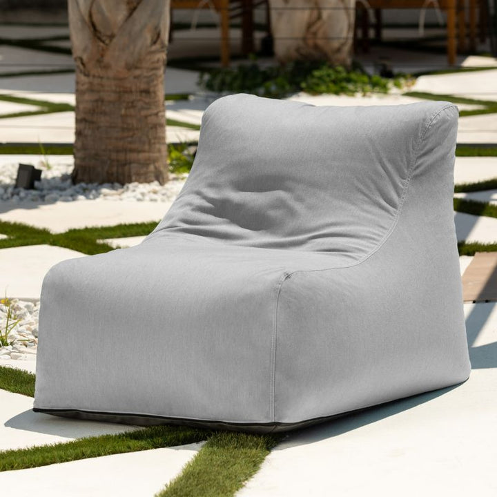 Jaxx Ponce Outdoor Bean Bag Chair in Sunbrella Granite in a palm-lined courtyard, a light grey Sunbrella bean bag chair