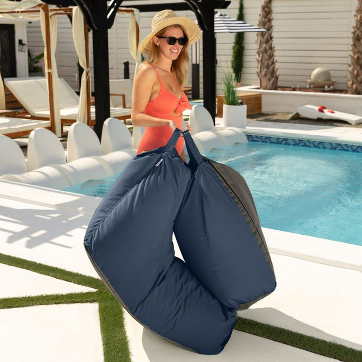 Woman carrying the folded Jaxx Prado outdoor bean bag lounger in Navy poolside