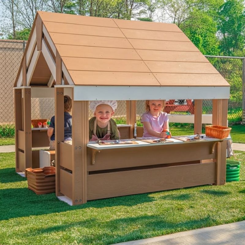 Smiling children enjoying pretend play at the activity table of the Whitney Brothers outdoorED Learning Pavilion, an outdoor classroom pavilion in a sunny, fenced play yard