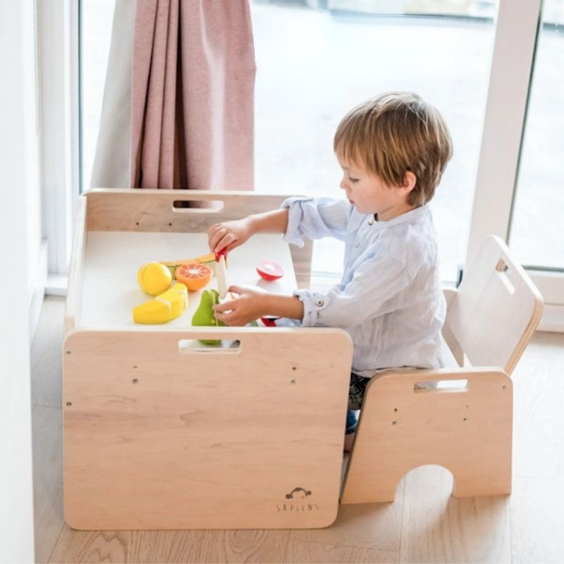 Child using the Sapiens Child Papaya Set Montessori weaning table from a side view, showing the correctly proportioned table and chair height for a child seated with feet flat on the floor