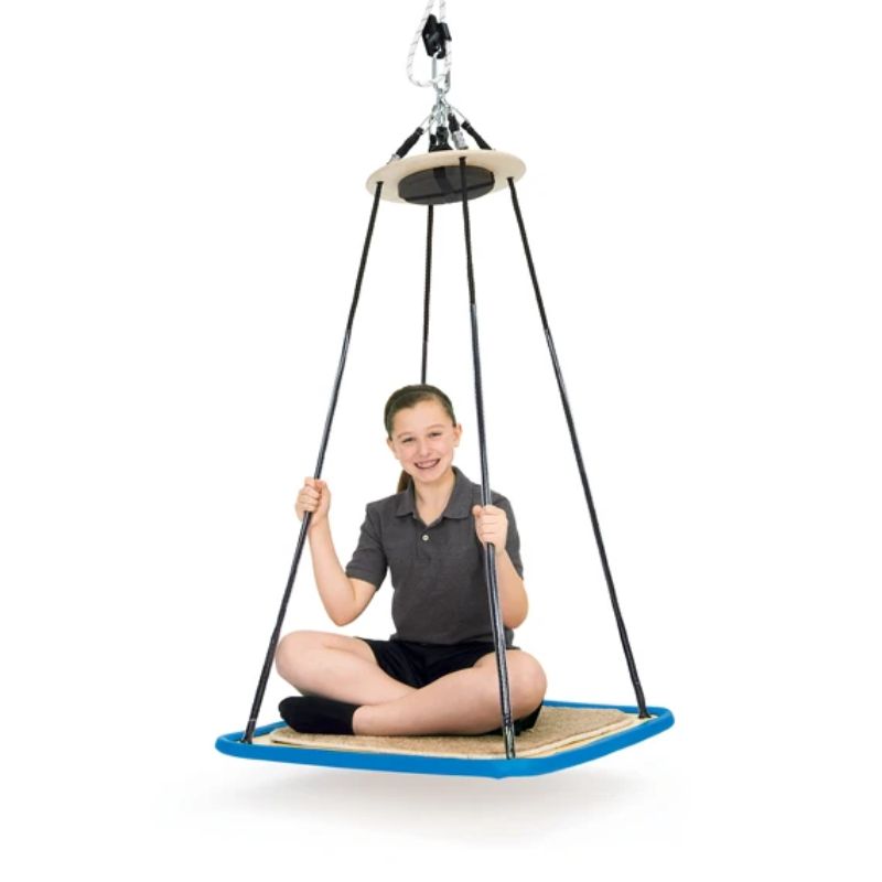 Smiling child sitting cross-legged on the carpeted Southpaw Platform Swing, holding the control lines beneath the top disc of this suspended swing for sensory integration therapy