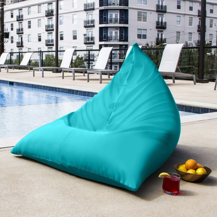 Jaxx Twist Outdoor Bean Bag Chair in Light Blue on a rooftop pool deck beside a cold drink and fruit bowl, a relaxed poolside lounger for shared outdoor spaces
