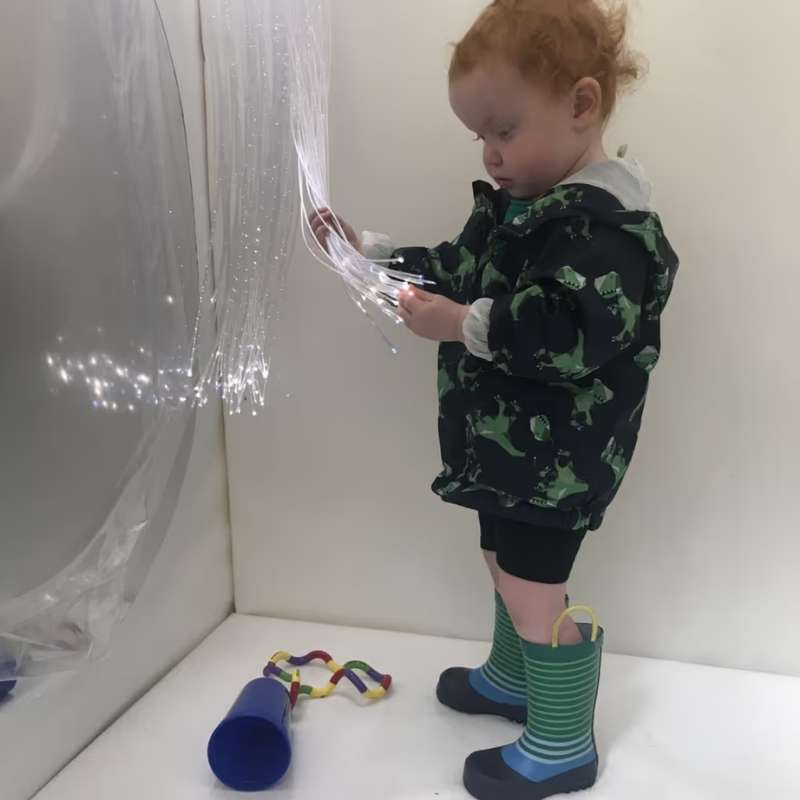A child holding illuminated Fiber Optic Tails, a compatible lighting accessory for the TFH Portable Sensory Den, sold separately