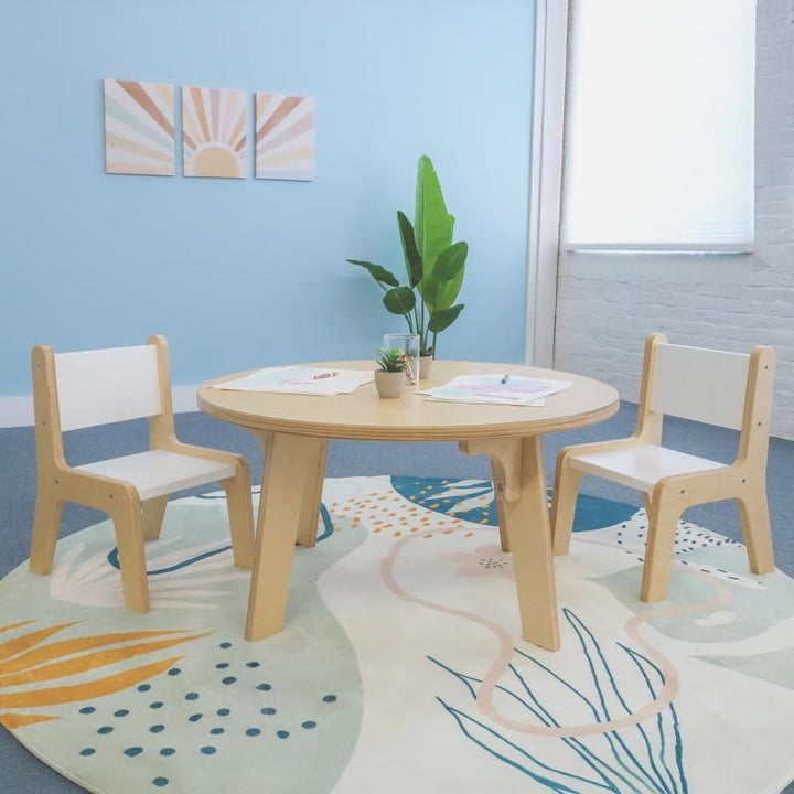 Whitney Brothers Whitney Plus Round Table at 18 inches high, a round classroom table with a maple top set with drawing paper and two children's chairs on a soft playroom rug