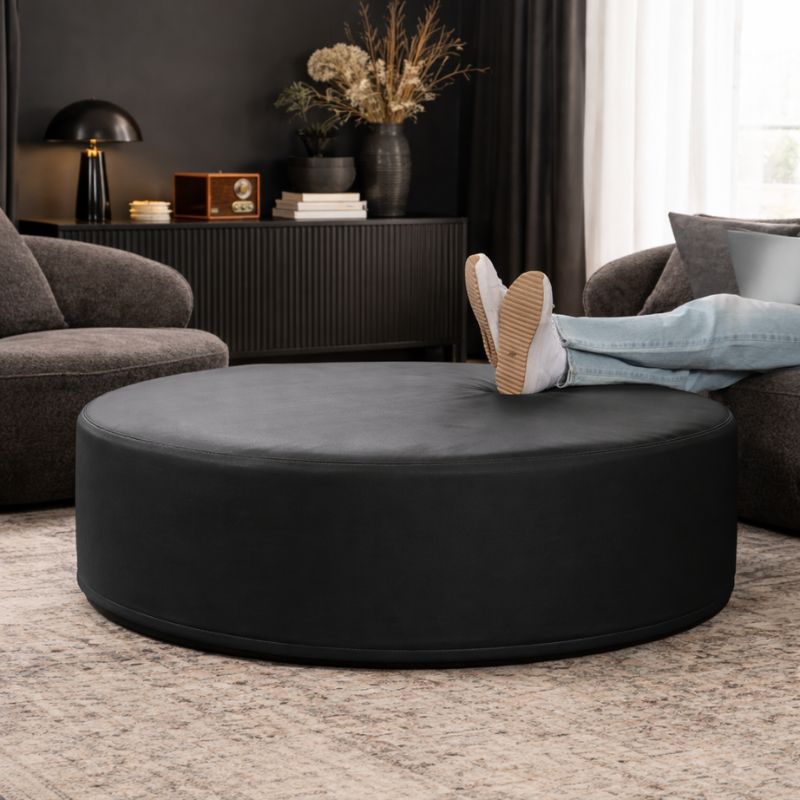 Jaxx Candler round ottoman in black, flexible foam seating styled in a moody living room setting