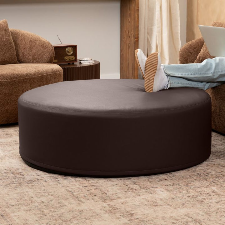 Jaxx Candler round ottoman in dark chocolate brown, flexible foam seating styled in a living room setting