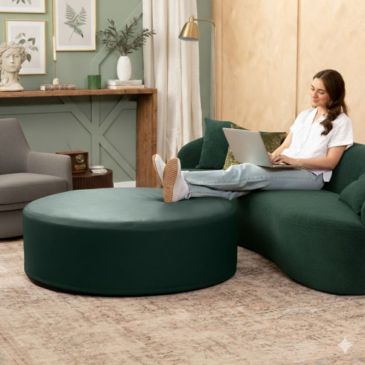 Jaxx Candler round ottoman in dark green, used as a coffee table alternative in a styled living room