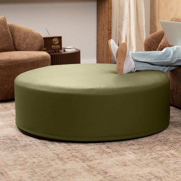 Jaxx Candler round ottoman in olive green, flexible foam seating styled in a living room setting