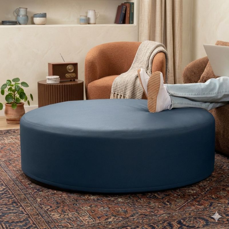 Jaxx Candler round ottoman in dark navy, flexible foam seating styled in a living room setting