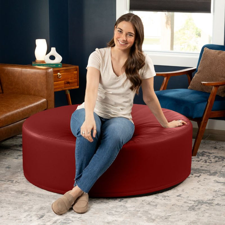 Woman seated on the Jaxx Candler round ottoman in red, showing the scale of this flexible foam seating
