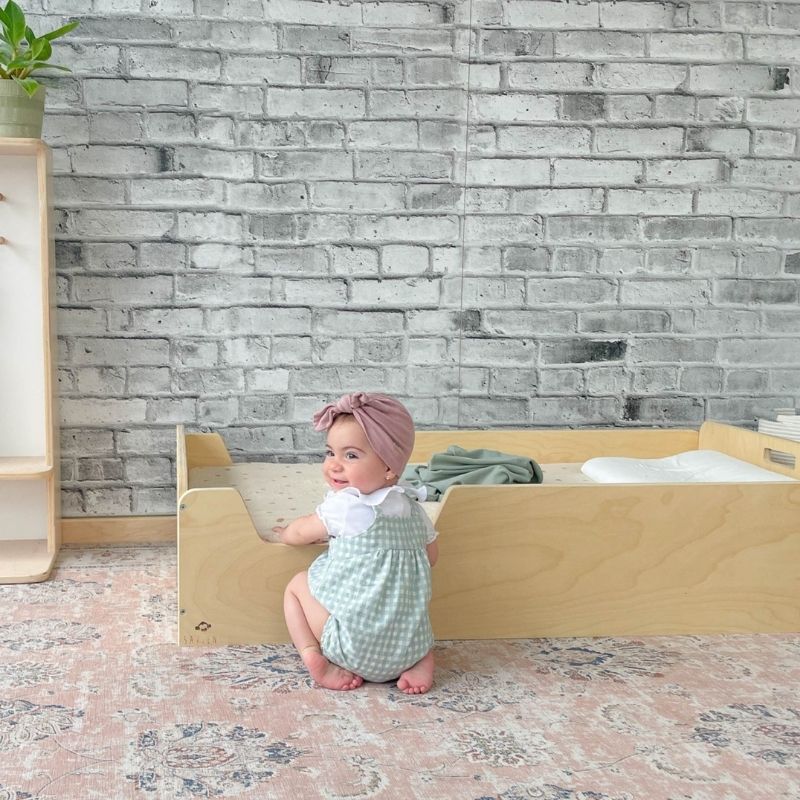 Child independently climbing into the Sapiens Child Apple Montessori floor bed with rails, showing the low-to-ground design that supports toddler independence and freedom of movement