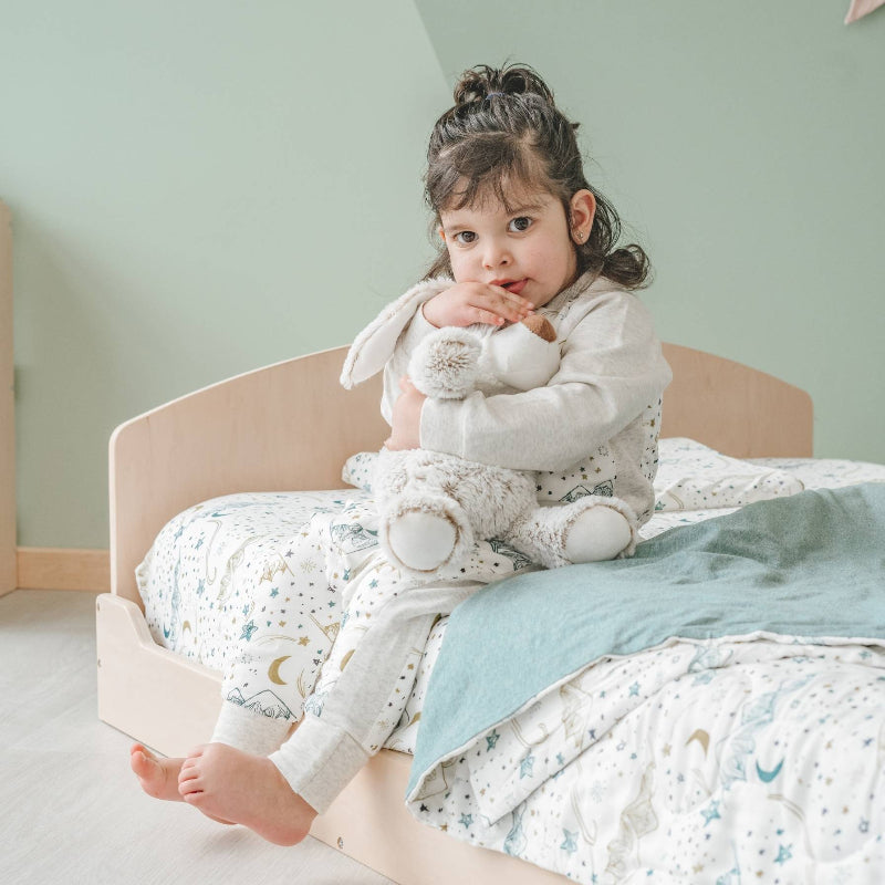 Close view of a child holding a stuffed toy on the Sapiens Child Cherry Montessori floor bed, showing the open accessible sleeping surface and rounded safety edges