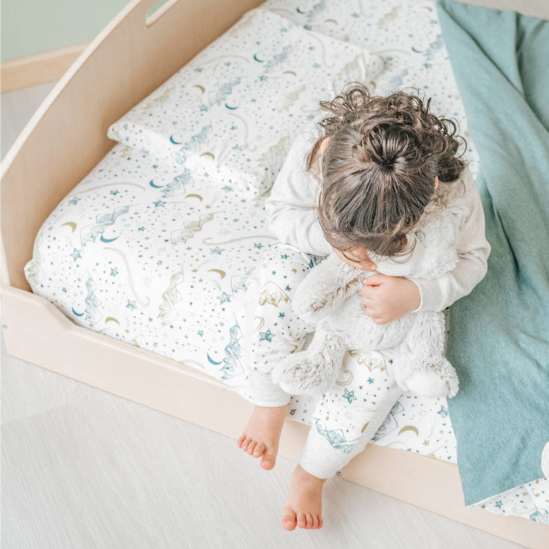 Child sitting on the Sapiens Child Cherry Montessori floor bed, showing the open low-profile frame that supports toddler independence and gross motor development
