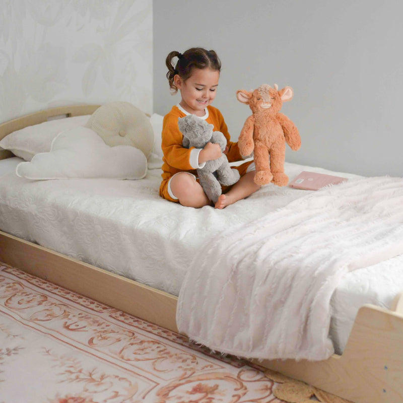 Child actively using the Sapiens Child Cherry Montessori floor bed in a lifestyle setting, showing the low-profile open twin design for independent sleep