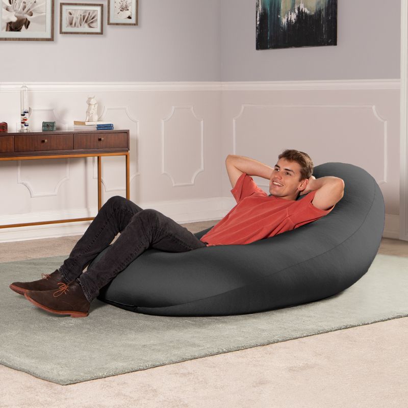 A man reclines in the black Jaxx Nimbus sensory bean bag chair, showing upright support for relaxing at home