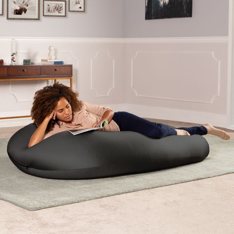 A woman reads a book lying across the black Jaxx Nimbus sensory bean bag chair, showing flexible sensory seating in a lounging position