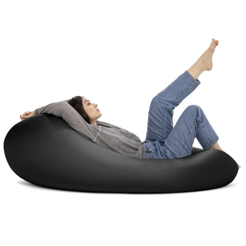 A woman reclines in the black Jaxx Nimbus sensory bean bag chair, showing the flexible seating chair in its flat position