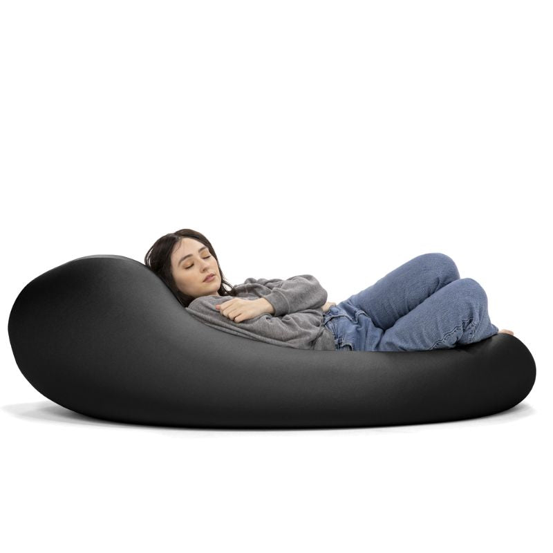 A woman rests in the black Jaxx Nimbus sensory bean bag chair, showing the stretchy spandex cover in a flat lounging position