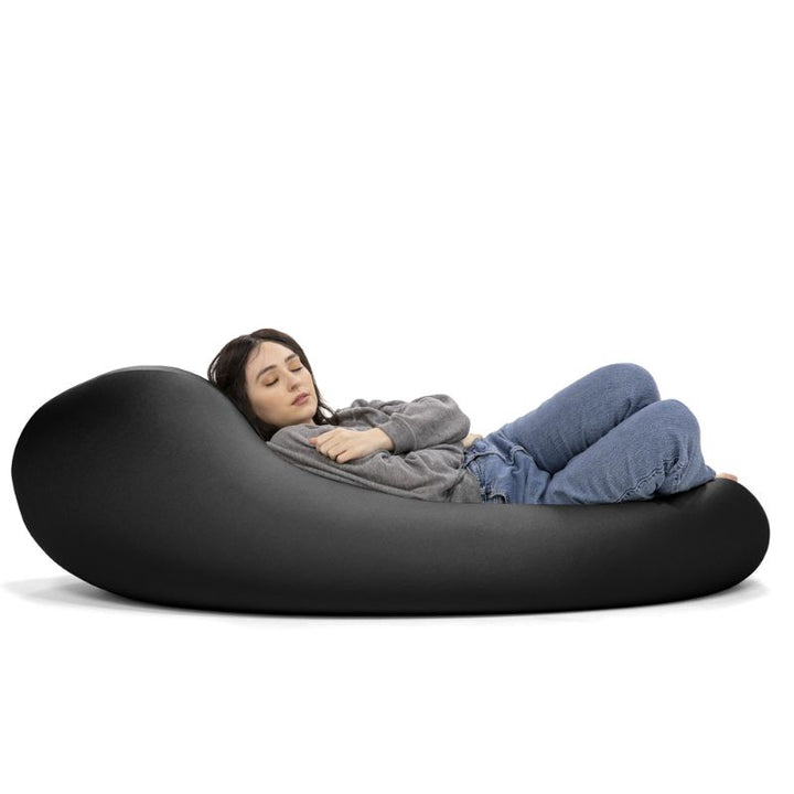 A woman rests in the black Jaxx Nimbus sensory bean bag chair, showing the stretchy spandex cover in a flat lounging position