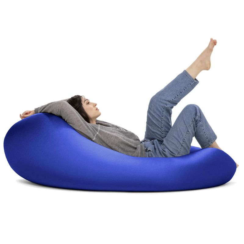 A woman reclines with her legs raised in the blue Jaxx Nimbus sensory bean bag chair, showing the stretchy cover in a relaxed lounging position