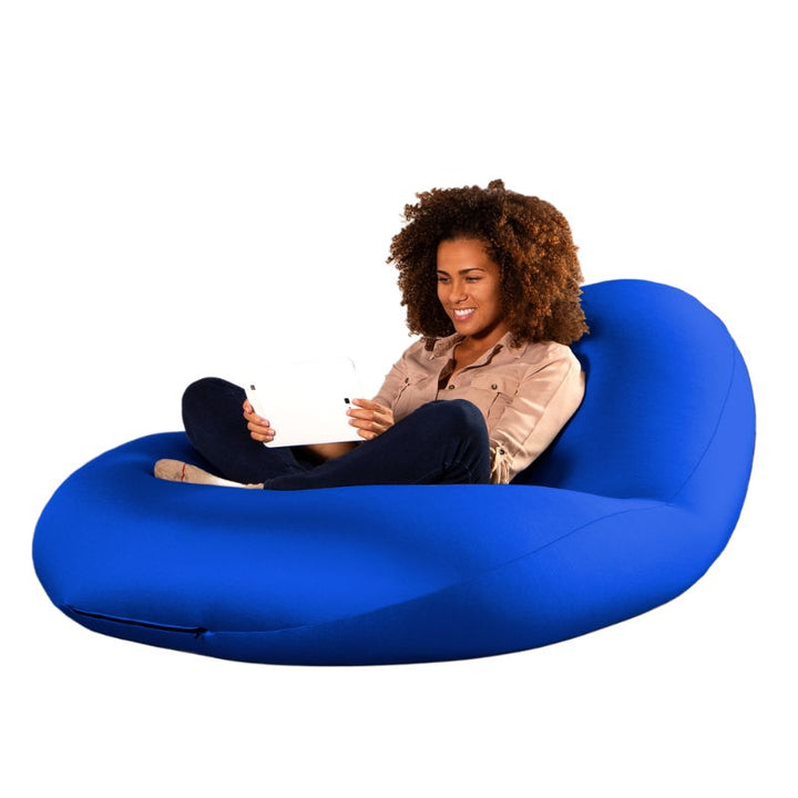 A woman sits cross-legged with a tablet in the blue Jaxx Nimbus sensory bean bag chair, demonstrating its upright seating support