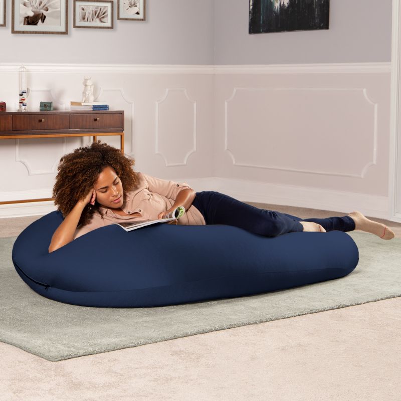A woman reads a book lying across the navy Jaxx Nimbus sensory bean bag chair, showing the stretchy cover in a lounging position