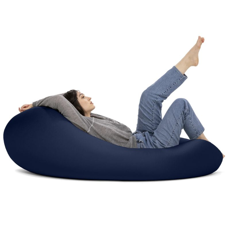 A woman reclines in the navy Jaxx Nimbus sensory bean bag chair, showing the stretchy spandex cover in its flat, flexible seating position