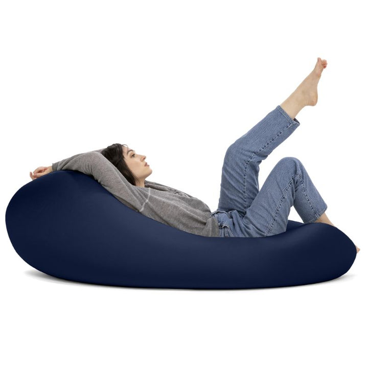 A woman reclines in the navy Jaxx Nimbus sensory bean bag chair, showing the stretchy spandex cover in its flat, flexible seating position