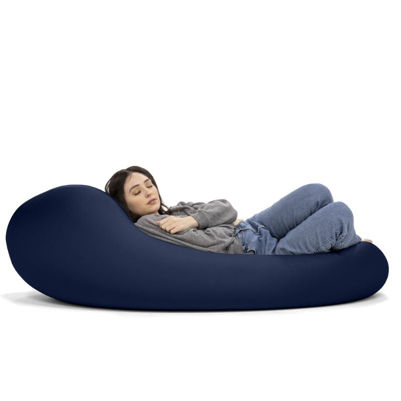 A woman rests in the navy Jaxx Nimbus sensory bean bag chair, showing the flexible seating chair in its flat lounging position
