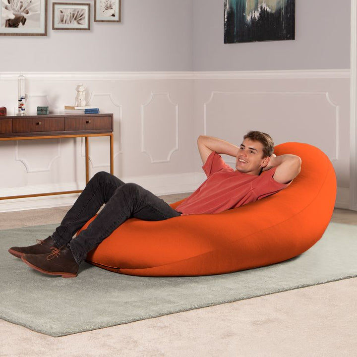A man reclines in the orange Jaxx Nimbus sensory bean bag chair, showing the stretchy cover as upright home seating