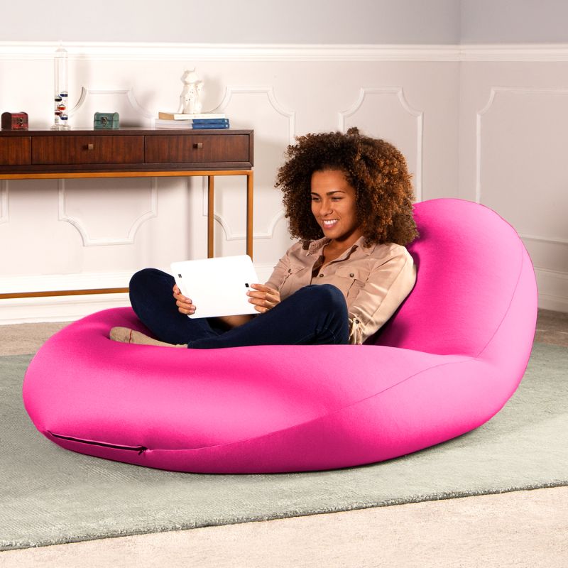 A woman sits with a tablet in the pink Jaxx Nimbus sensory bean bag chair in a living room, showing flexible seating for home use