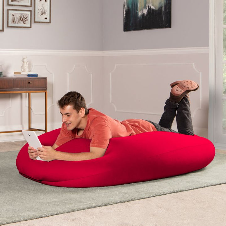 A man lies on the red Jaxx Nimbus sensory bean bag chair using a tablet, showing the stretchy cover in a lounging position