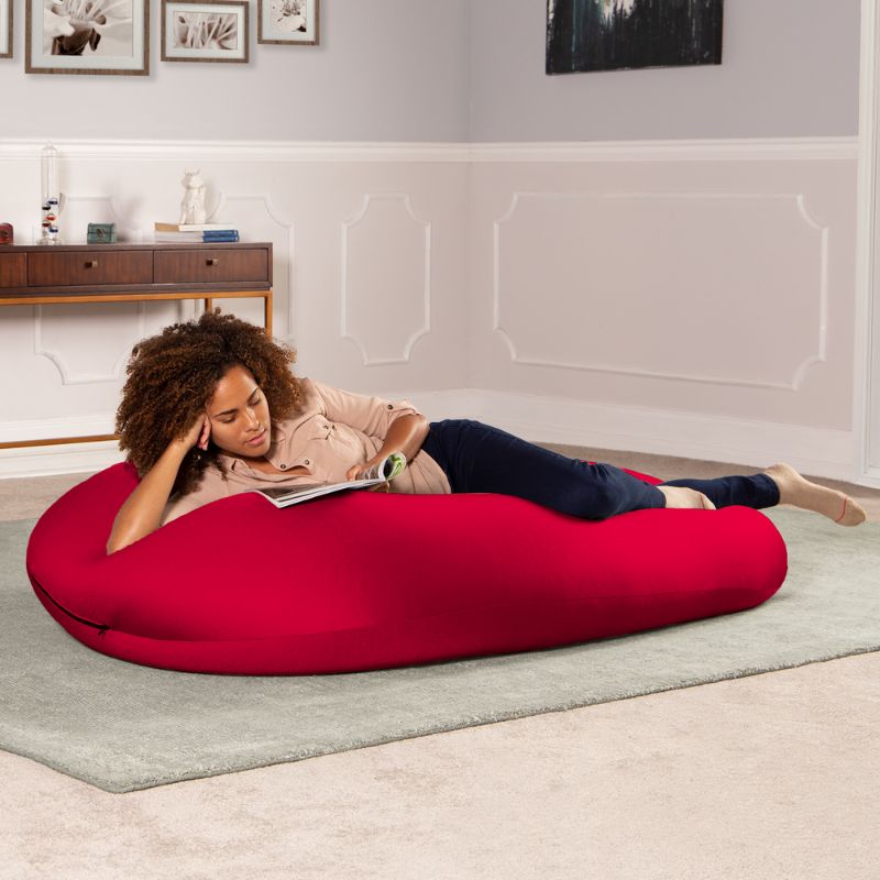 A woman reads a book lying across the red Jaxx Nimbus sensory bean bag chair, showing flexible sensory seating in a lounging position