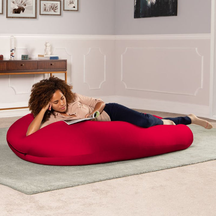 A woman reads a book lying across the red Jaxx Nimbus sensory bean bag chair, showing flexible sensory seating in a lounging position