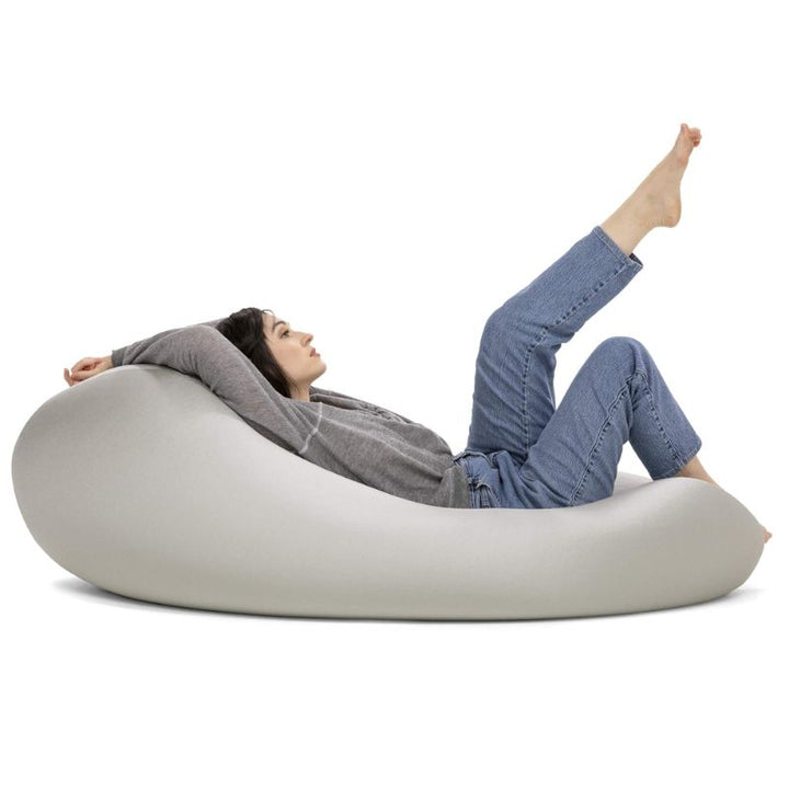 A woman reclines with her legs raised in the light gray Jaxx Nimbus sensory bean bag chair, showing the stretchy cover in a relaxed lounging position