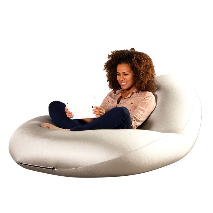 A woman sits cross-legged with a tablet in the white Jaxx Nimbus sensory bean bag chair, showing upright flexible seating for classrooms and homes