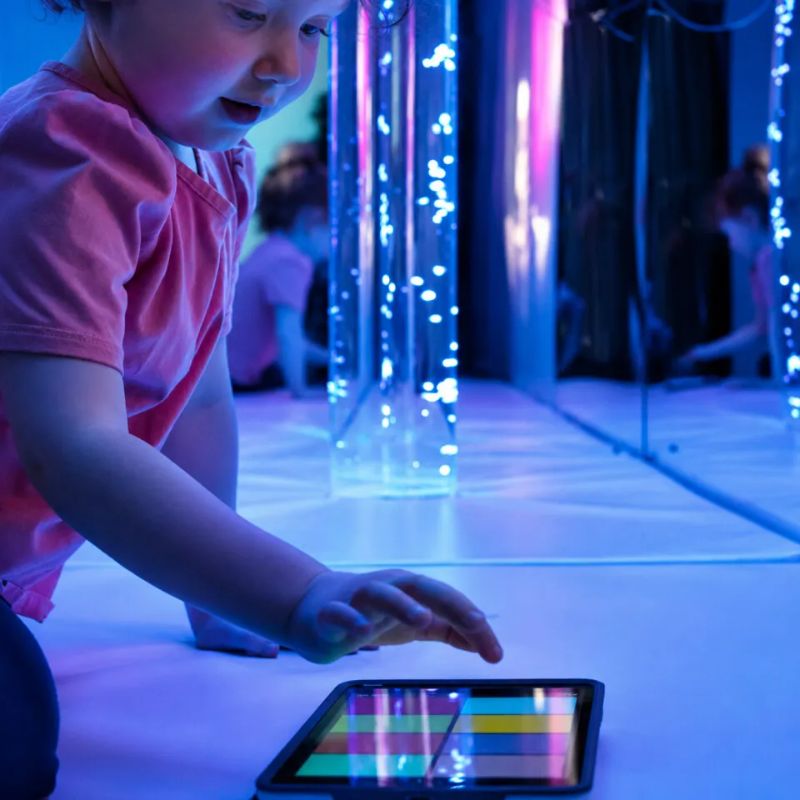 Toddler tapping a colour panel on a tablet to control the TFH Genie System Bubble Tube, an interactive sensory bubble tube for cause-and-effect play