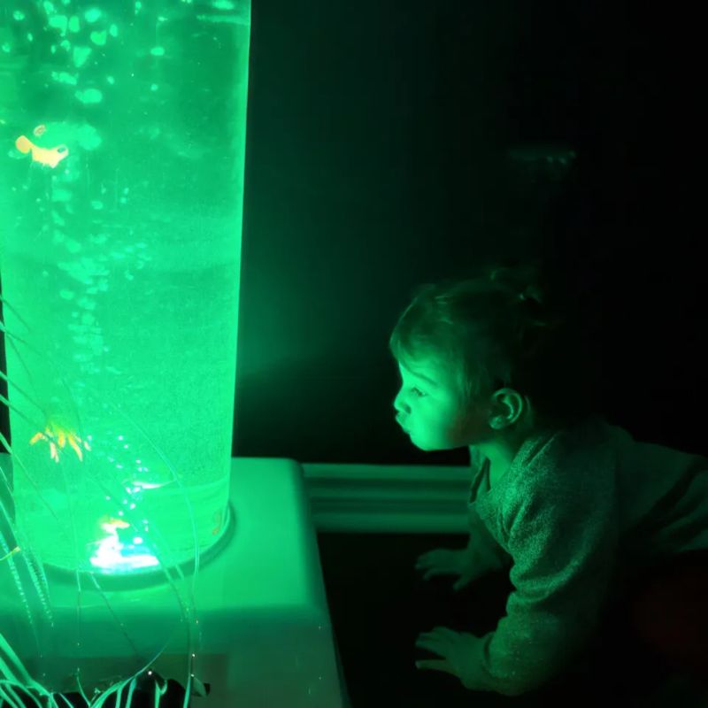 Toddler gazing up at the glowing green TFH Giant Water Bubble Tube 8 inch wide, a large sensory bubble tube with floating fish for calming visual exploration