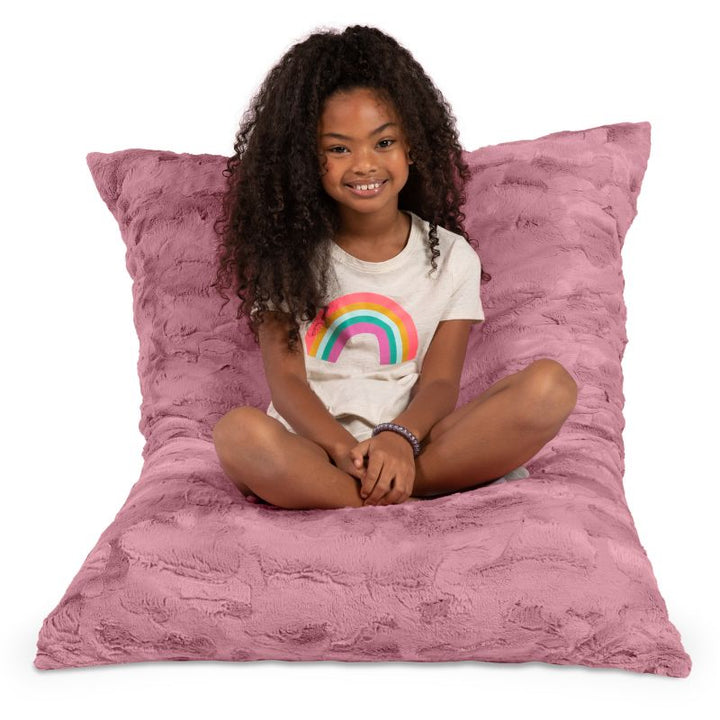 Girl seated cross-legged on the CrashPuff by Raven-Symoné sensory floor lounger in Wild Rose
