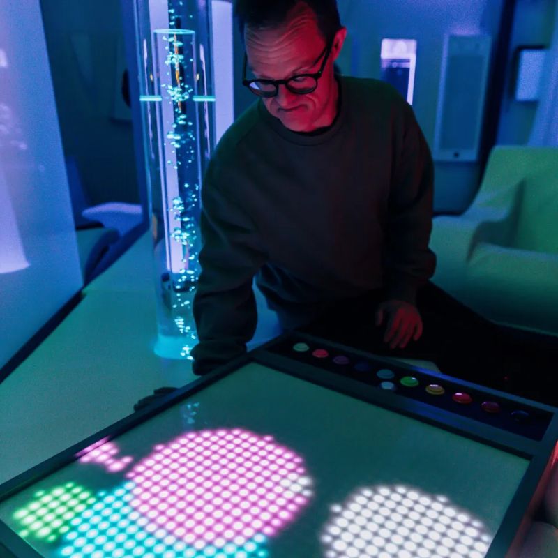 Adult watching pink, green and white light circles bloom across the TFH Pixels Pro Illumination Panel, an LED sensory light panel for multi-sensory rooms