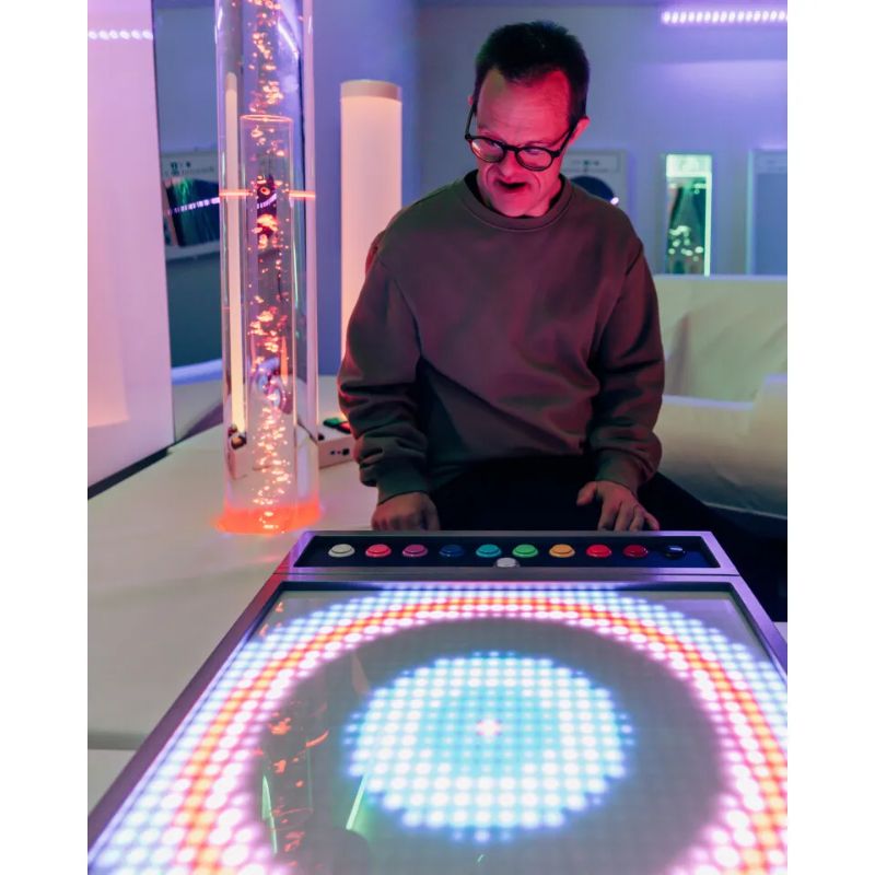 Smiling adult using the TFH Pixels Pro Illumination Panel to create a glowing circular pattern, an interactive sensory light panel for all ages and abilities