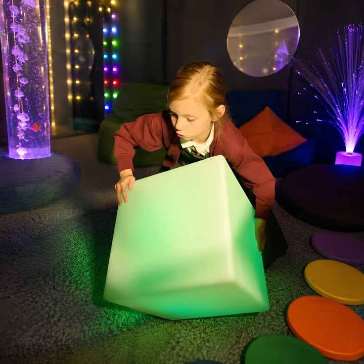 TFH Mood Dice sensory mood cube glowing green as a child lifts it in a multi-sensory room with bubble tubes and fibre optic lights