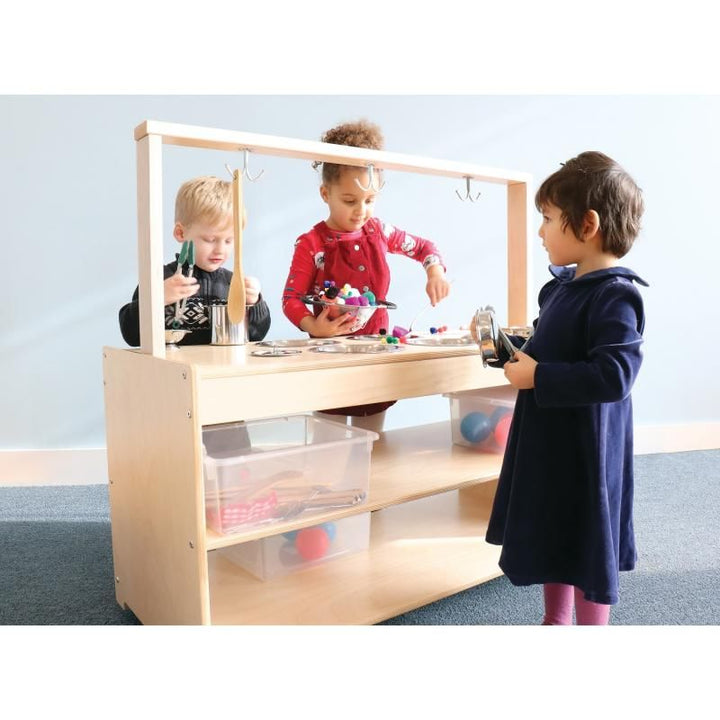 Children exploring pouring and scooping at the Whitney Brothers Mobile Sensory Play Kitchen, a play kitchen sensory table with clear storage bins on its open shelves