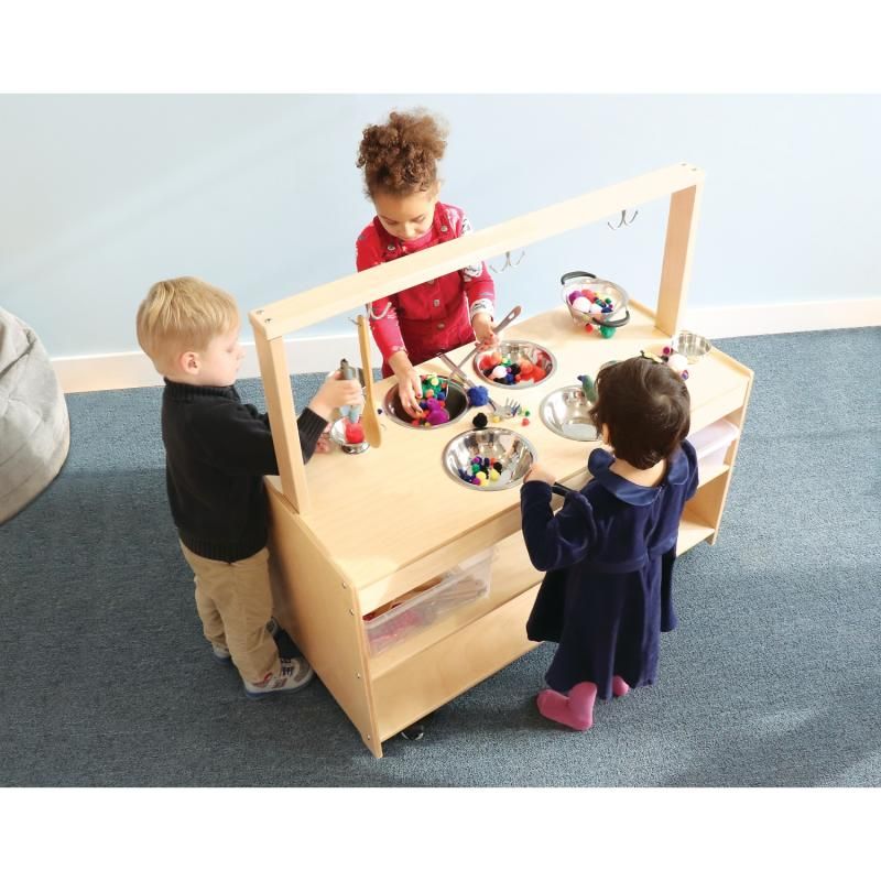 Three children using tongs to sort colorful pom-poms in the stainless steel bowls of the Whitney Brothers Mobile Sensory Play Kitchen during group sensory table play