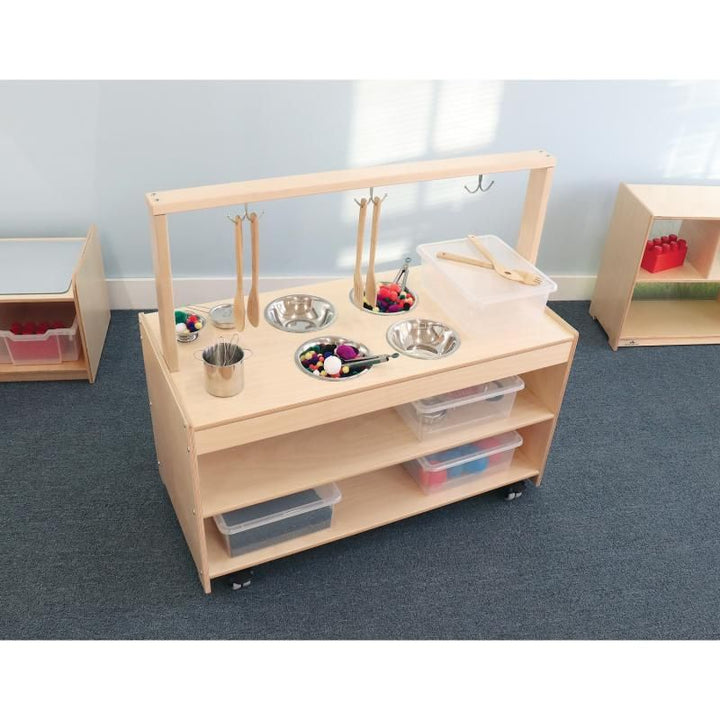 Angled view of the Whitney Brothers Mobile Sensory Play Kitchen in an early learning classroom, with pom-poms in the mixing bowls ready for tactile sensory play
