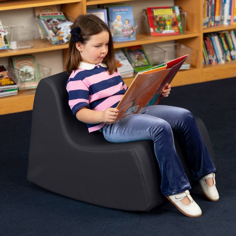 A child reading in the black Jaxx Midtown Rocker, a sensory rocking chair for kids in a school library